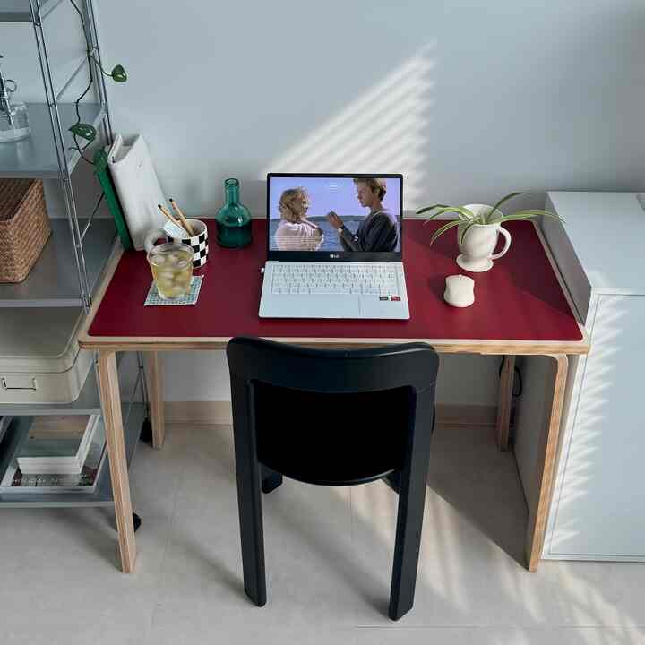 深い赤のレザーマットが敷かれたモダンなホームオフィスのデスクと黒い椅子が配置されたシンプルな空間