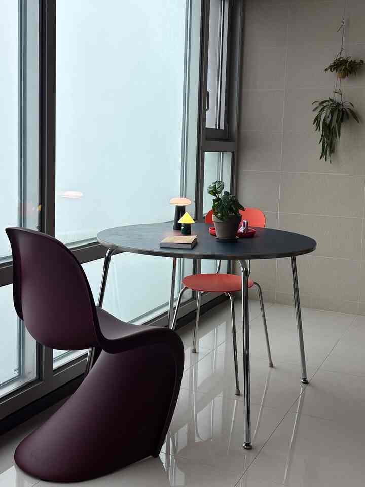 ブラックテーブルとコーラル色および紫の椅子があるナチュラルカラーのモダンなダイニングルーム、大きな窓際に植物が配置された清潔感のある空間