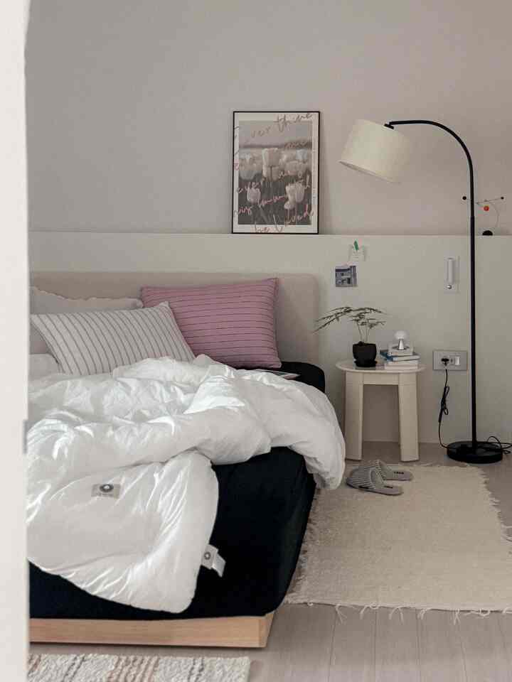A white and black toned bedroom featuring a cozy bed, floor lamp, nightstand, and rug in a natural modern interior style