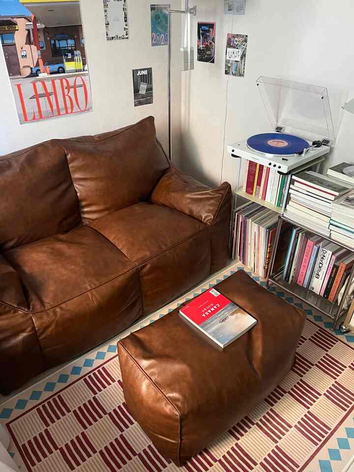 ヴィンテージブラウン調のリビング、2人用ビーズクッションソファとオットマン、LPターンテーブルとサイドテーブルが配置された温かみのあるインテリア