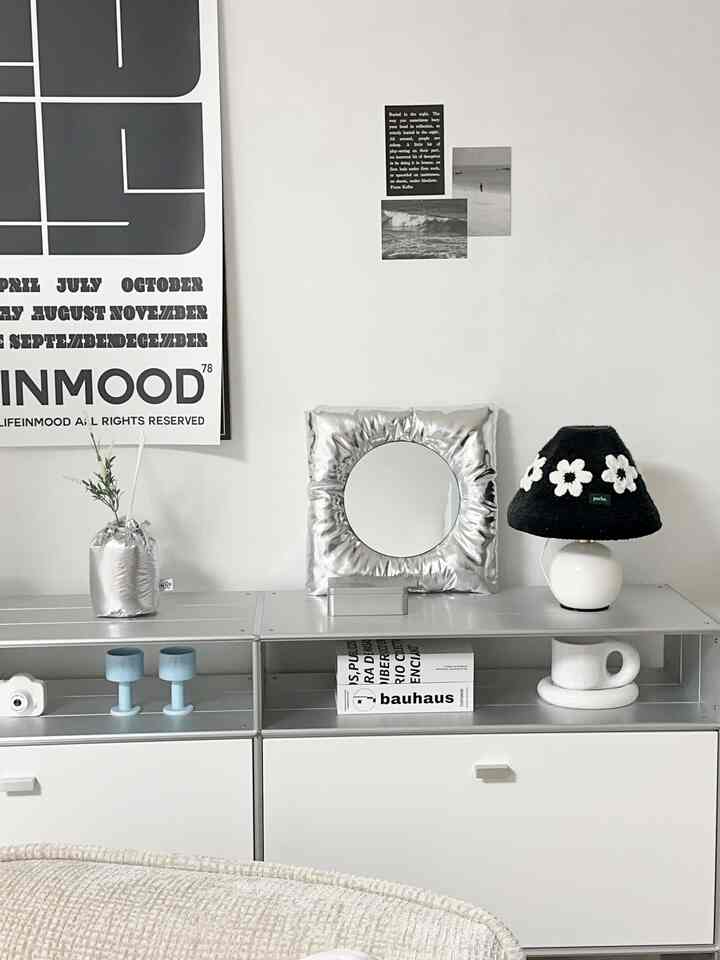 Minimal modern living room in white and silver tones featuring a cushion mirror and floral lamp on a sleek sideboard