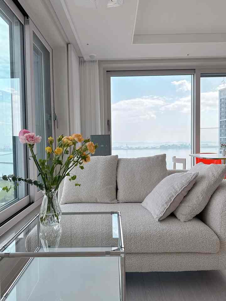 白とモノトーンのリビング、中央に白いソファと左側のガラスサイドテーブル上の色鮮やかな花瓶が配置された清潔感のある空間