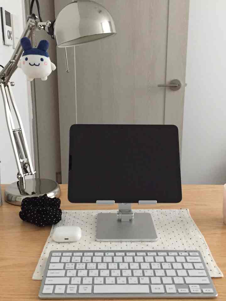 白い壁と木製のデスクがあるホームオフィス、ミニキーボードとデスクランプが配置された整った作業空間