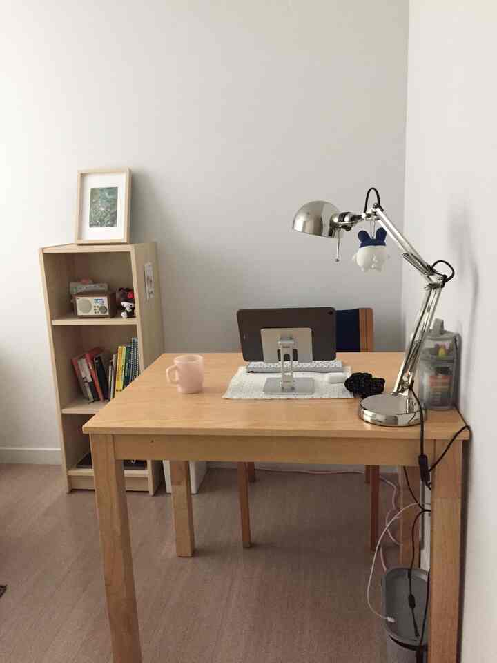 白を基調としたワンルーム、木目調の机と本棚が配置された清潔感のある雰囲気のホームオフィス