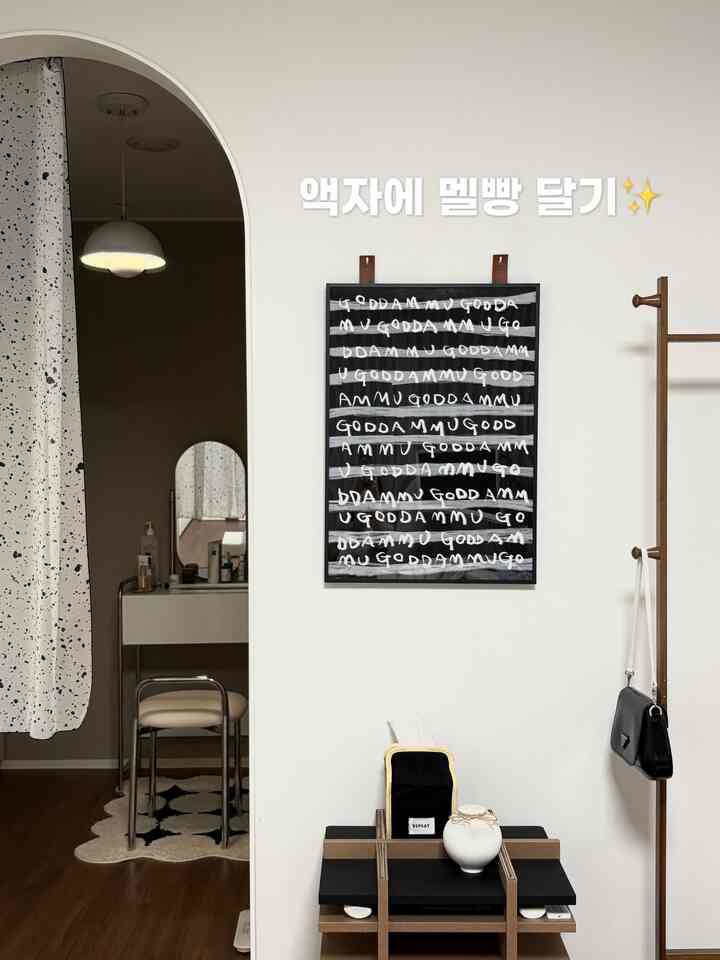 白い壁と木目調の床、アーチ扉とレザーストラップで額縁を掛けた、シンプルで温かみのあるインテリア