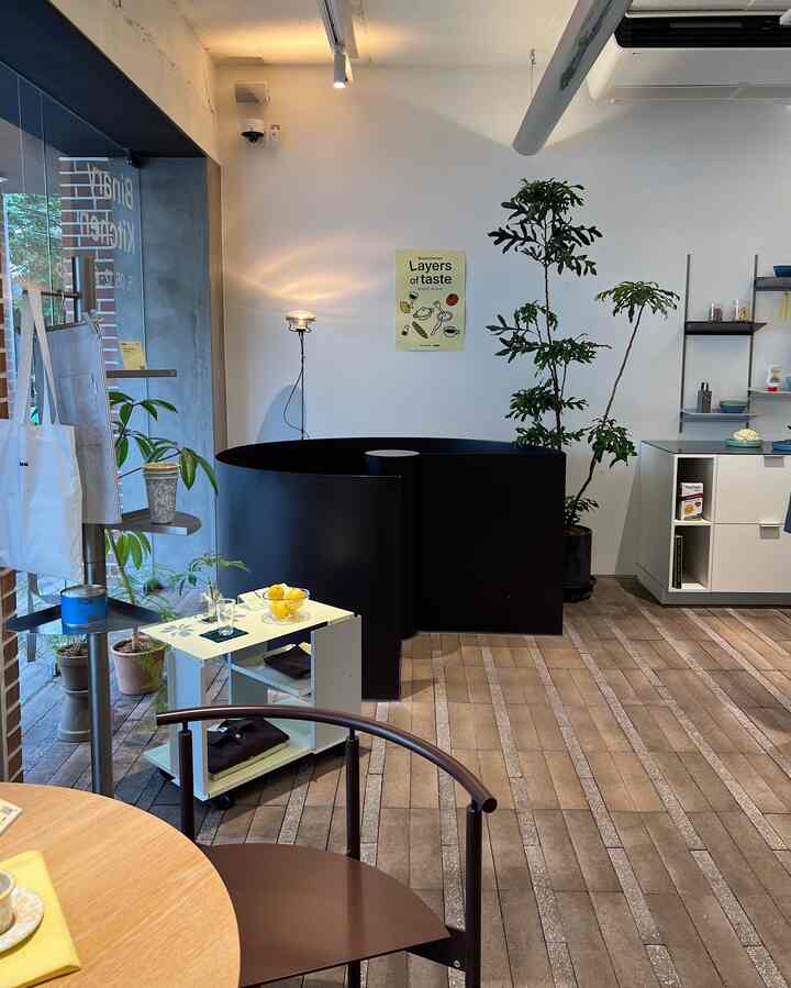ナチュラルな木目調と白い壁のカフェ風空間、ダイニングテーブルや植物、照明が配置された雰囲気のあるインテリア