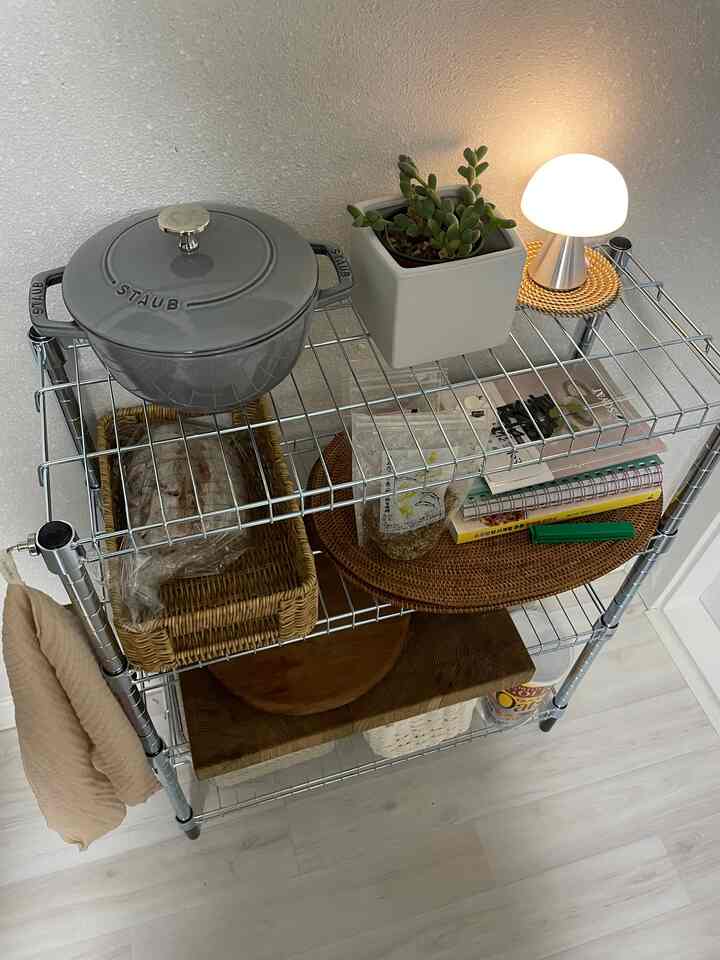 ナチュラルな色調のキッチン多段棚、鍋、植物、LEDランプ、バスケットが配置された印象的な空間