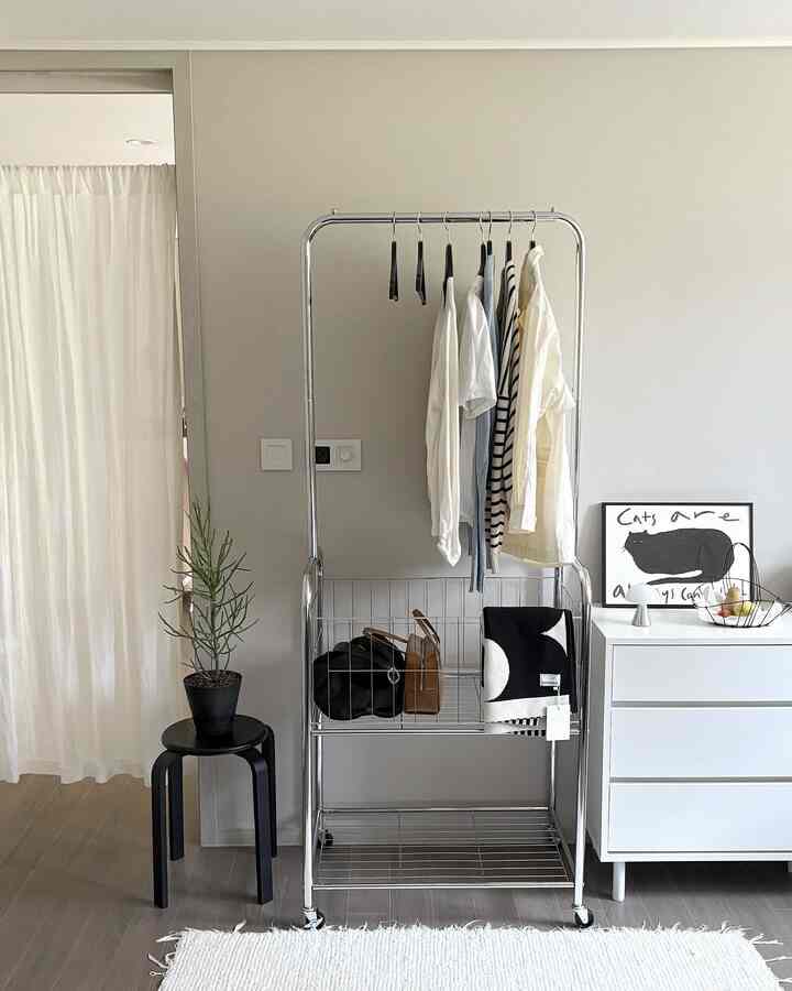 White and silver-toned bedroom featuring a central movable storage hanger with shelves, creating a clean and modern look