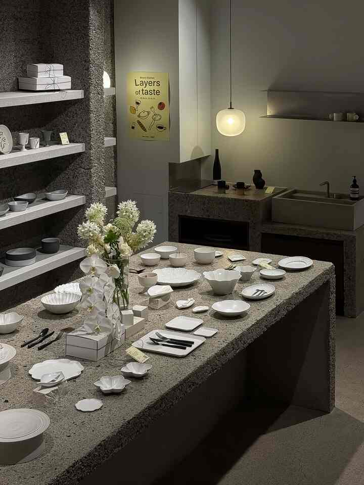 白を基調としたナチュラルモダンなキッチンスペース、コンクリートのダイニングテーブルに多様な白い食器と花瓶が配置された落ち着いた雰囲気のインテリア