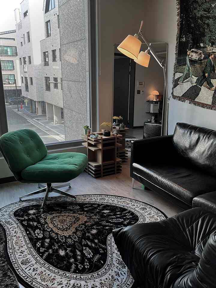 A modern-retro living room featuring a green chair and black leather sofa with a patterned black rug and floor lamp