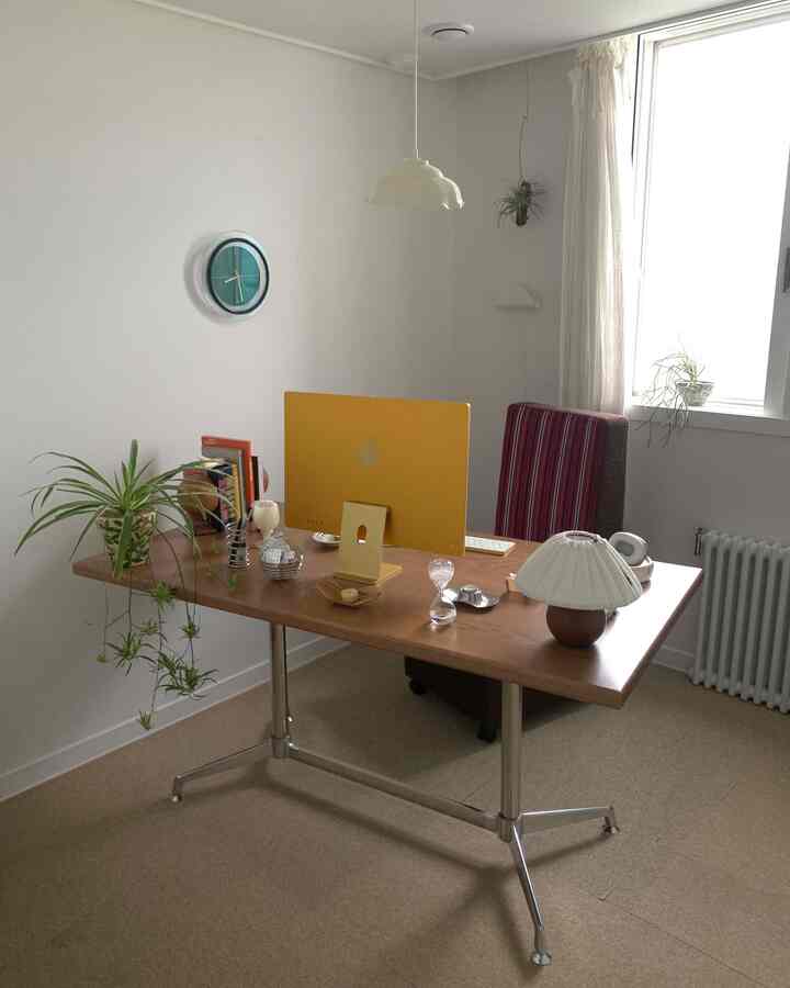 白い壁とブラウンの机、植物とモダンなオフィスチェアが配置された落ち着いたホームオフィス空間