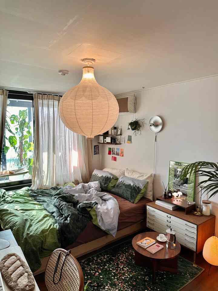 木目調とナチュラルカラーの調和した寝室、植物と鏡が配置された温かみのある空間