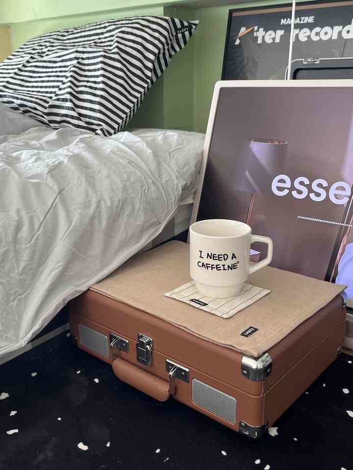 White and brown toned bedroom featuring pillows and a coffee mug on a small table, creating a cozy atmosphere