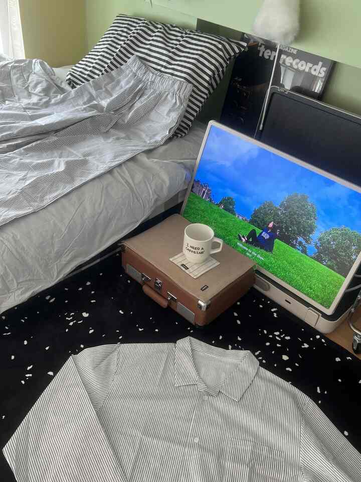 白と黒のトーンの寝室、ストライプ柄の寝具とモニタースタンド、ホームカフェの雰囲気を醸し出すマグカップが配置された落ち着いた空間