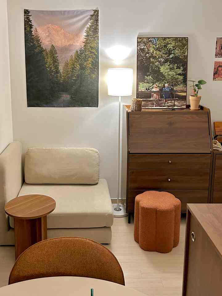 ベージュとブラウンの色調のワンルームリビング、木製家具とブークレチェア、フロアランプが配置された雰囲気のある空間