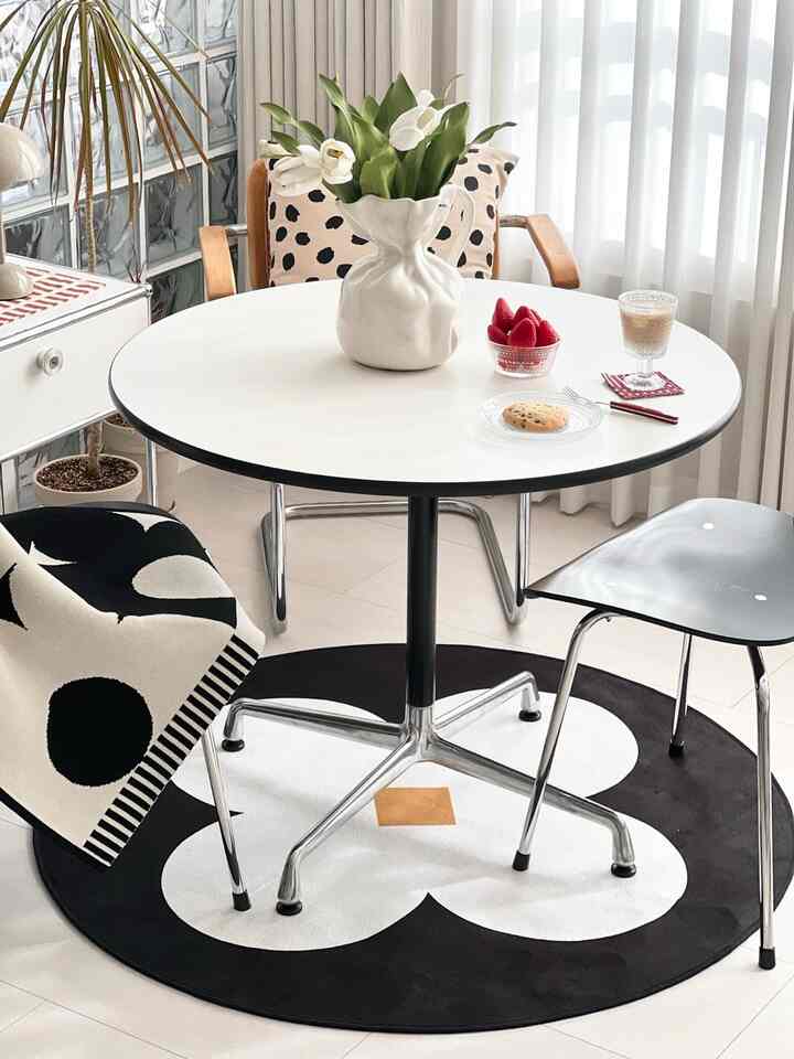白と黒のミッドセンチュリーモダンなダイニング、丸いラグとテーブル上の花瓶が配置された印象的な空間