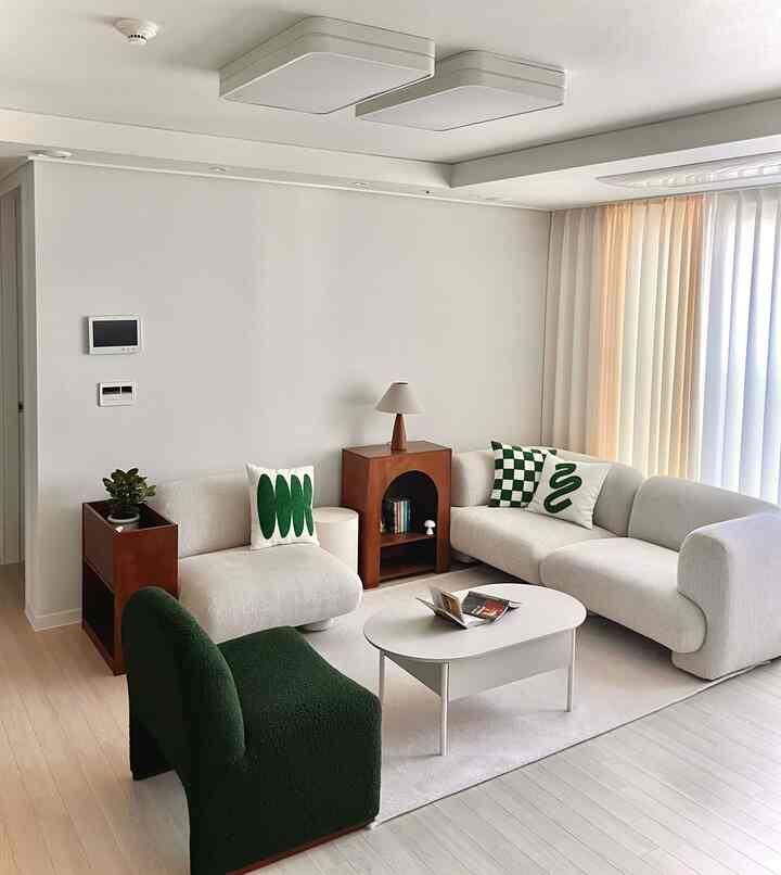 ホワイトと木目調が調和したシンプルモダンなリビング、アイボリーファブリックソファとダークグリーンのアームチェアが配された温かみのある空間