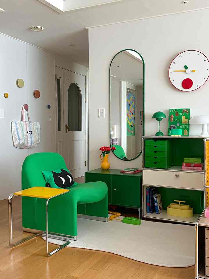 白い壁と木目調の床が特徴のリビング、緑のモジュール家具と椅子が配置された雰囲気のある空間