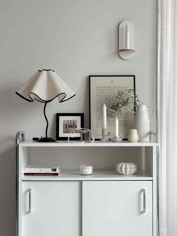 白とベージュの色調のリビング、サイドテーブルにキャンドル、ポスター、黒の額が置かれたシンプルでクラシックな雰囲気のインテリア