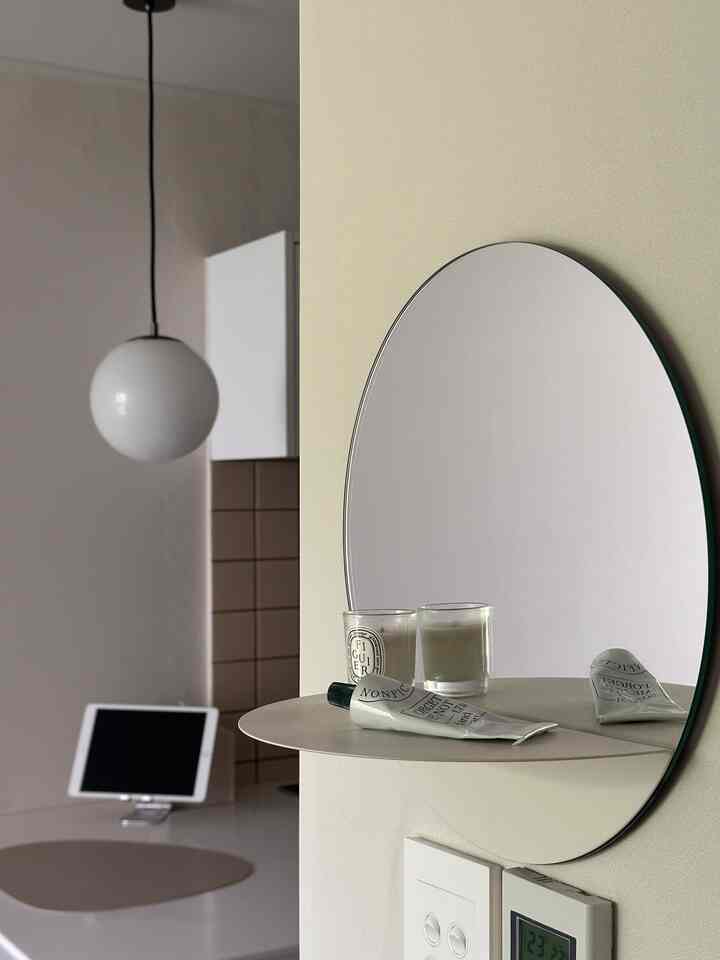 柔らかなホワイトとベージュの寝室空間、丸い壁鏡とミニマルなキャンドルが置かれたシンプルなインテリア