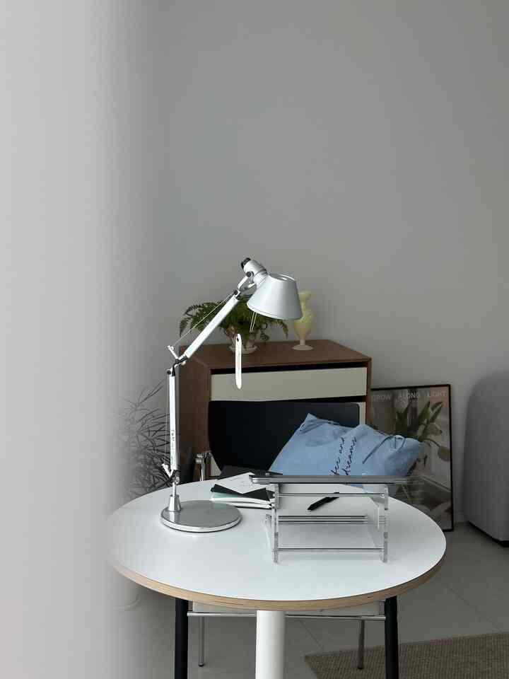 A white and brown toned home office featuring a round table and an adjustable table lamp in a simple setting