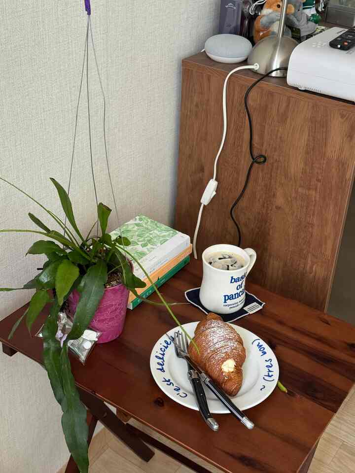 木目調のテーブルと白い壁が調和したおうちカフェ空間、緑の植物がアクセントとして配置されている雰囲気のあるインテリア。