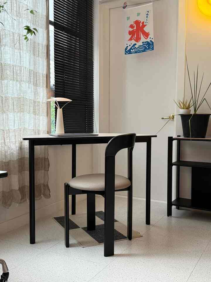 A small home office space with white walls and floor and black furniture, featuring a neat and simple layout