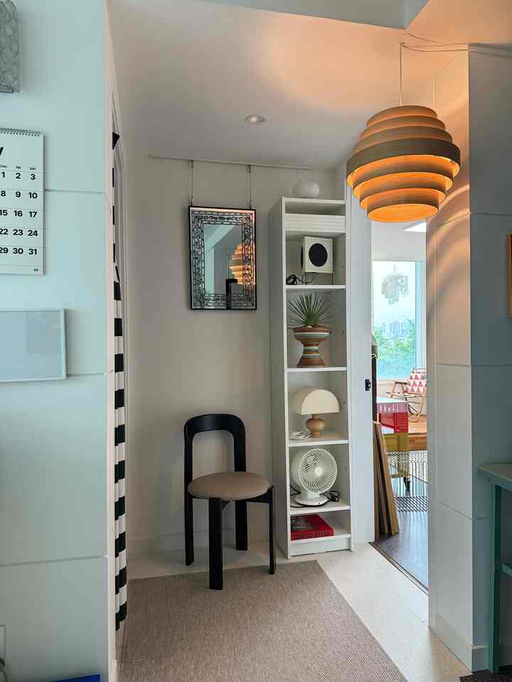 Natural-toned small living room corner with white and beige colors featuring a black chair, corner shelving, and wooden pendant lighting