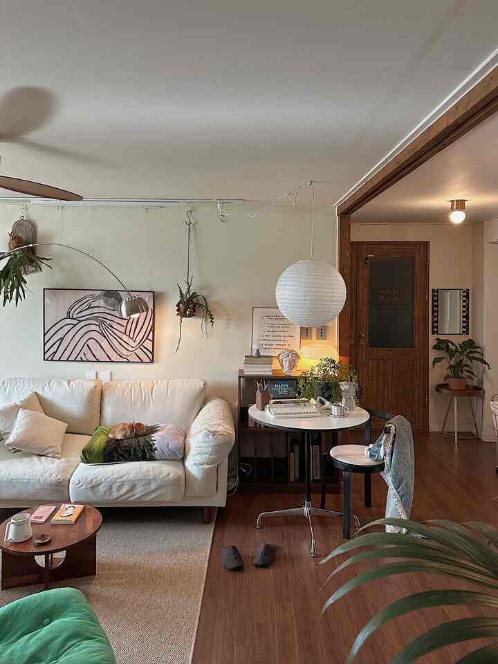 Living room in white and wood tones featuring a round table, sofa, and various plants with cozy vintage atmosphere