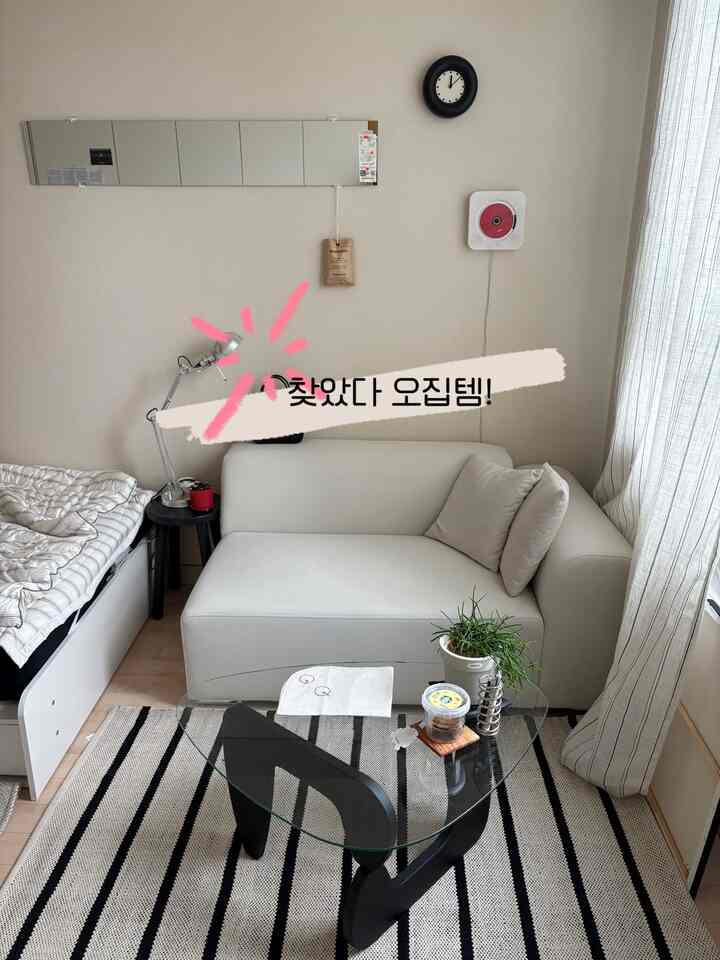 明るくナチュラルな色調のワンルーム、ベージュのソファとストライプのラグ、シンプルなサイドテーブルが配置された落ち着いたインテリア