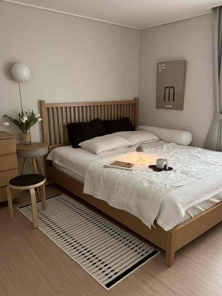 Natural-toned bedroom featuring wooden bed, stool, and nightstand in white walls, creating a simple and warm atmosphere