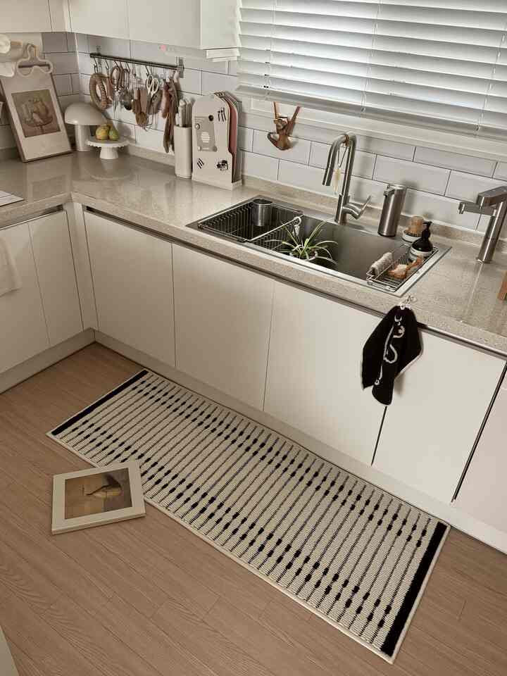 Modern and clean kitchen featuring white cabinets and wood tone flooring, with a sink and various kitchen utensils arranged neatly