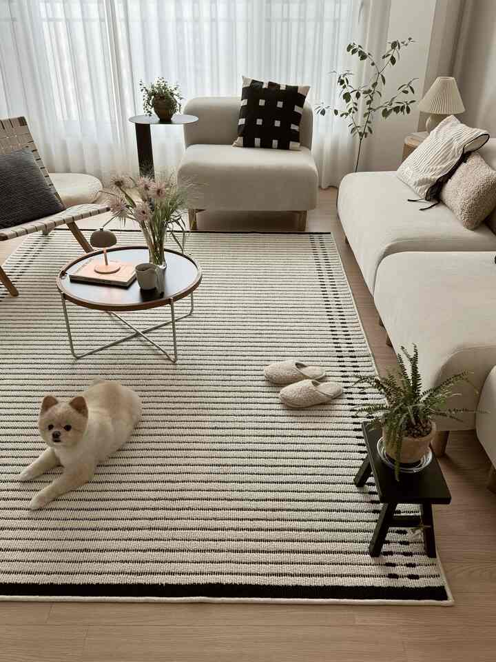 明るいアイボリー調のリビング、快適なソファとストライプのラグが配置され、自然な雰囲気の中で犬がくつろいでいるインテリア