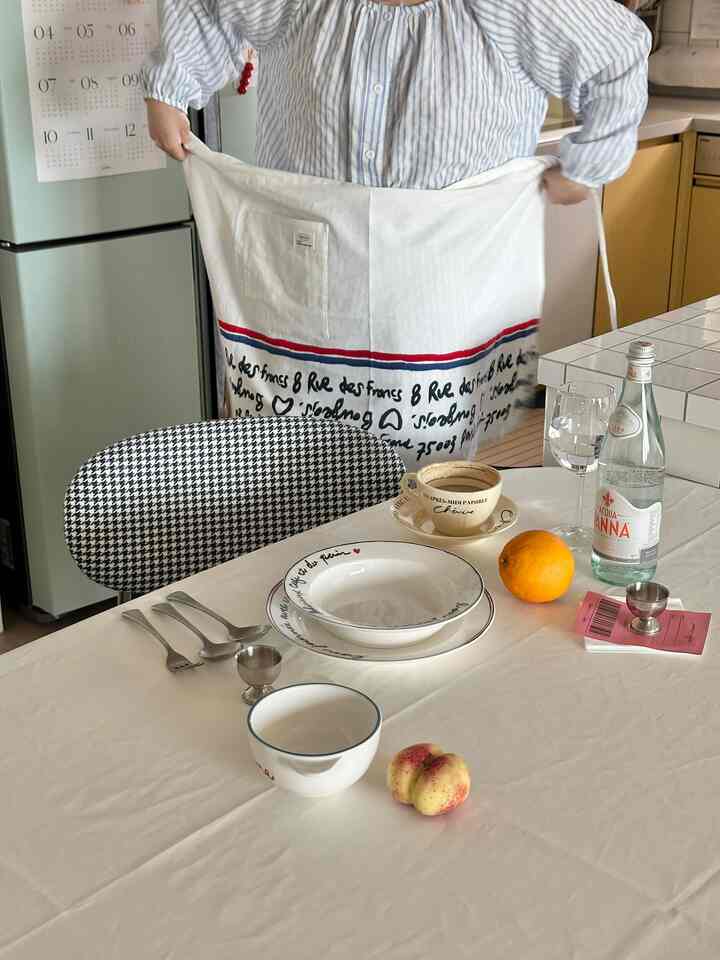 ホワイトのテーブルクロスと黒白のパターン椅子があるキッチンのダイニングスペース、コーヒーカップと果物が置かれた温かみのあるおうちカフェの雰囲気