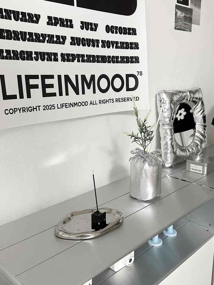 シルバー調のリビングルーム、棚の上にトレイ、ディフューザー、額縁、ウォールデコが配されたモダンな空間