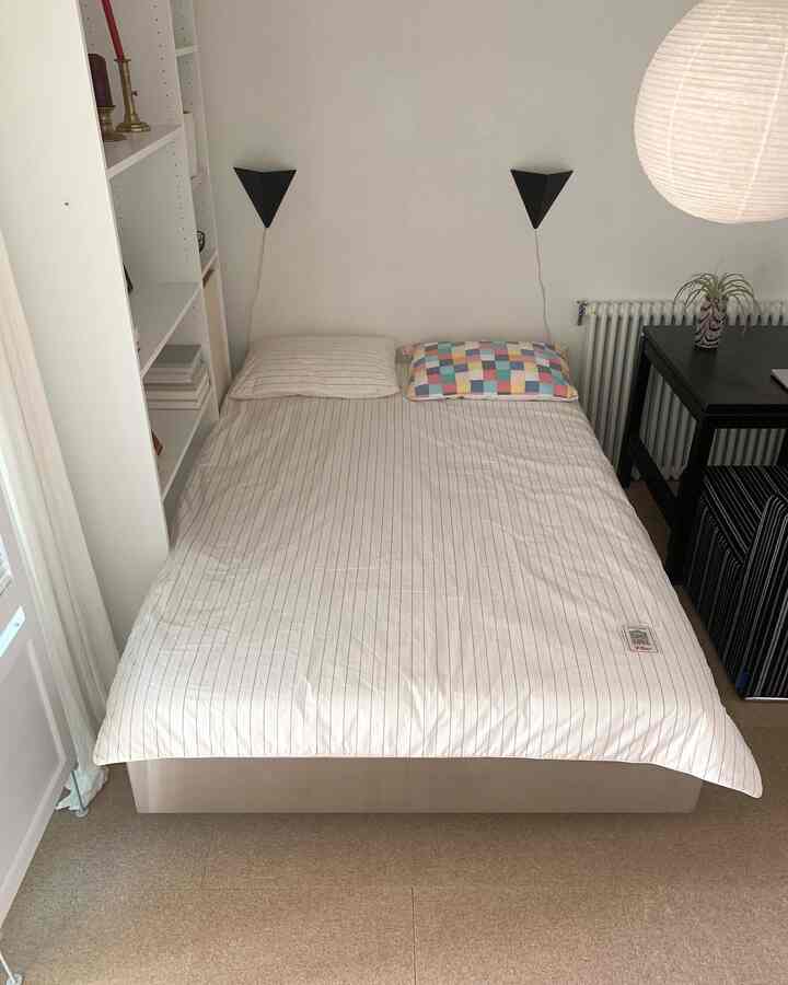 白とナチュラルカラーの寝室、ベッドと枕が中央に配置されたシンプルで居心地の良い空間