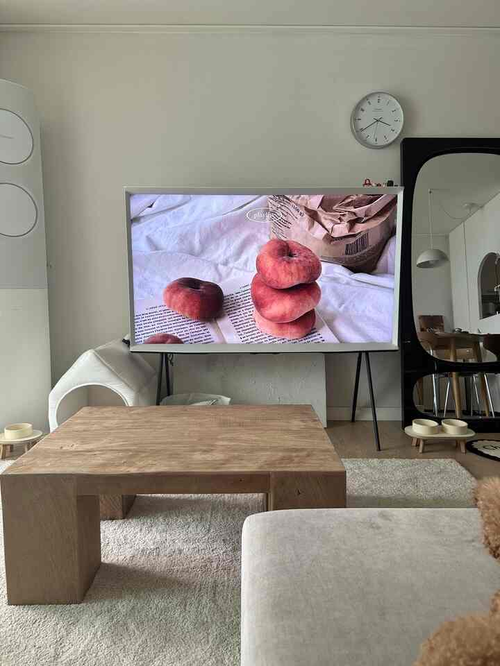 ナチュラルな木目調とホワイトのリビング、中央に大きな古材テーブルとサムスンのセリフテレビ、全身鏡、ペット用食器が配置された雰囲気のあるインテリア