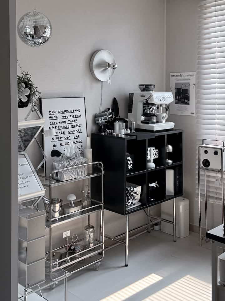 A mid-century modern home cafe space with white walls and floors, featuring a black cubical shelf and metal gap shelving trolley
