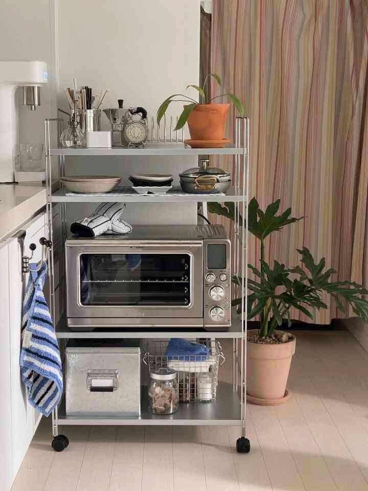 白とシルバーのトーンのキッチン空間、ステンレス棚と整然とした調理器具、オーブンが配置されたシンプルなキッチン