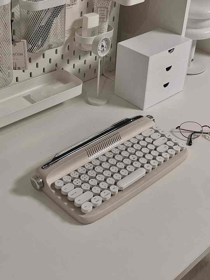 白を基調としたホームオフィスのデスク、レトロスタイルのキーボードと整理収納が配置された印象的な空間