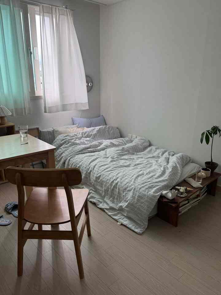 白と木目調の6畳の寝室、低いベッドと木製のデスク、ダイニングチェアが自然で落ち着いた印象の空間