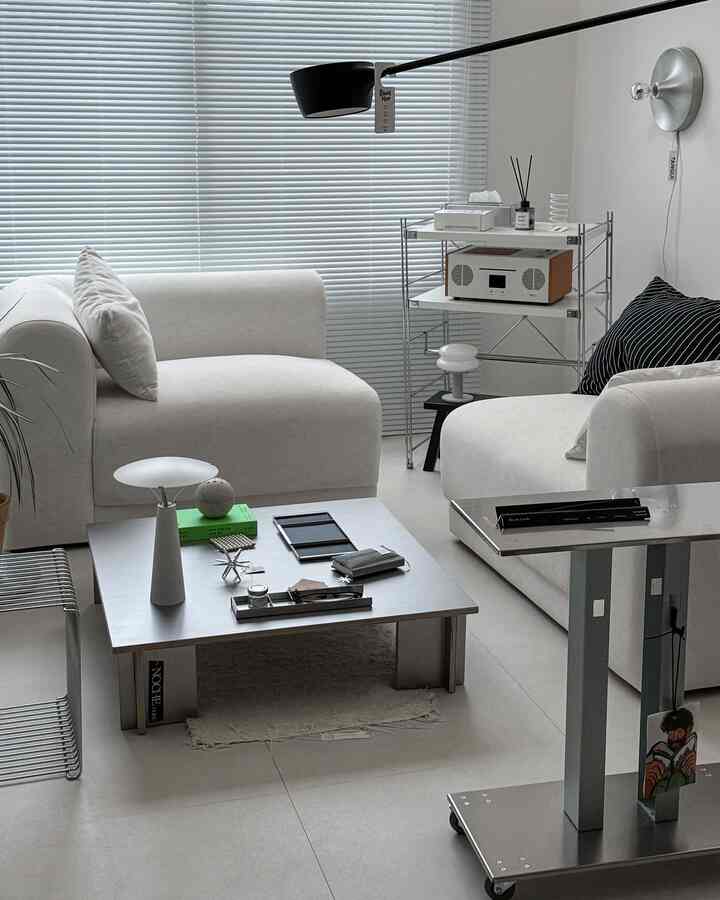 白とシルバーのトーンのリビング、二つのソファとコーヒーテーブル、ブラインドが配置されたモダンで清潔感のあるインテリア