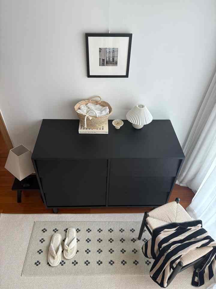 明るい白い壁とチャコール色のキャビネットがあるナチュラルモダンなウォークインクローゼット、ラグとスツールが配置された整理整頓された空間