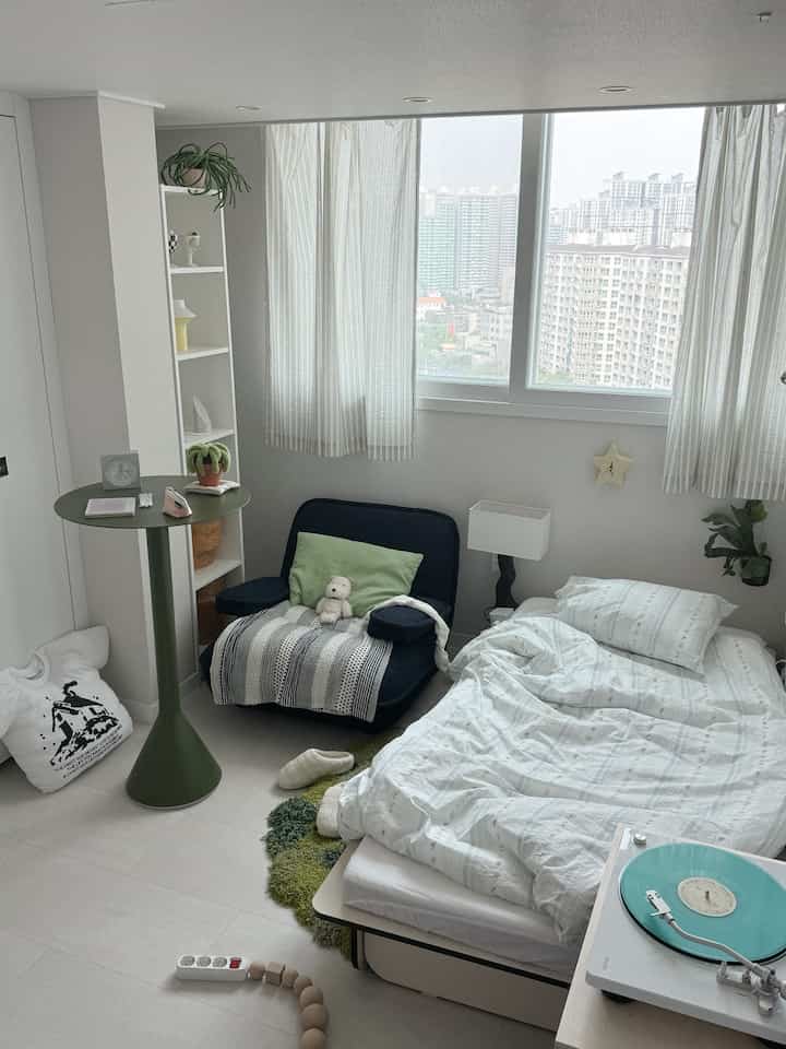 白とネイビーのトーンが特徴的な小さな寝室、ベッドとアームチェアが配置された落ち着いた雰囲気のインテリア