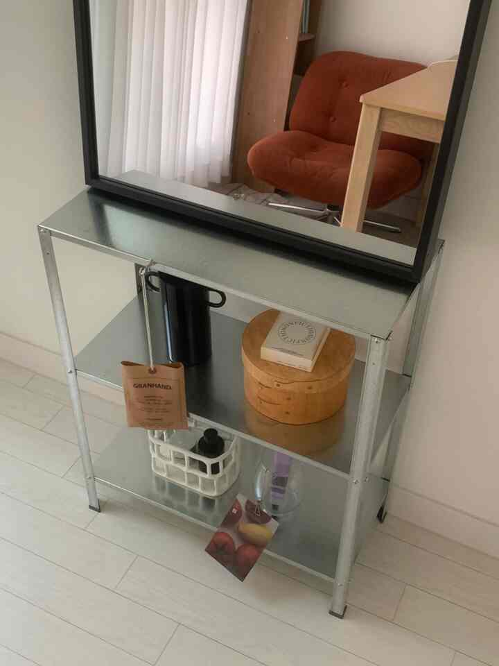 白い壁と床、スチール製の棚、レンガ色の椅子、ナチュラルな木製テーブルが配置されたワンルームインテリア