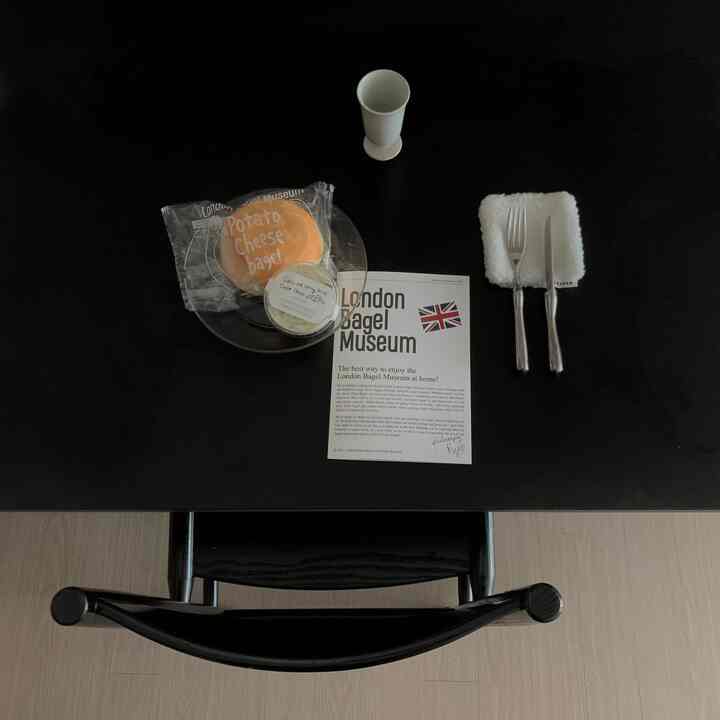 黒い木製テーブルの上に透明な皿とポテトチーズベーグル、カトラリーが置かれたシンプルなダイニングスペース