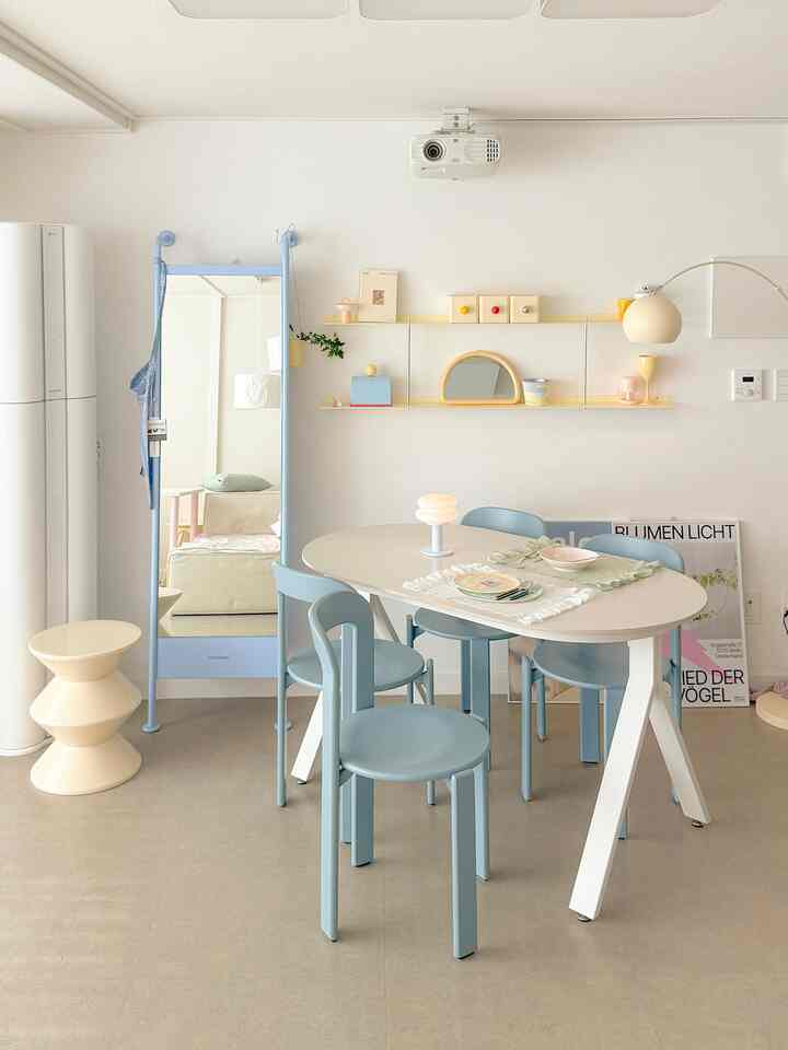 明るいホワイトとスカイブルーの色調のリビング、白いオーバルのダイニングテーブルに青い椅子が4脚、全身鏡とフロアランプが調和する印象的な空間