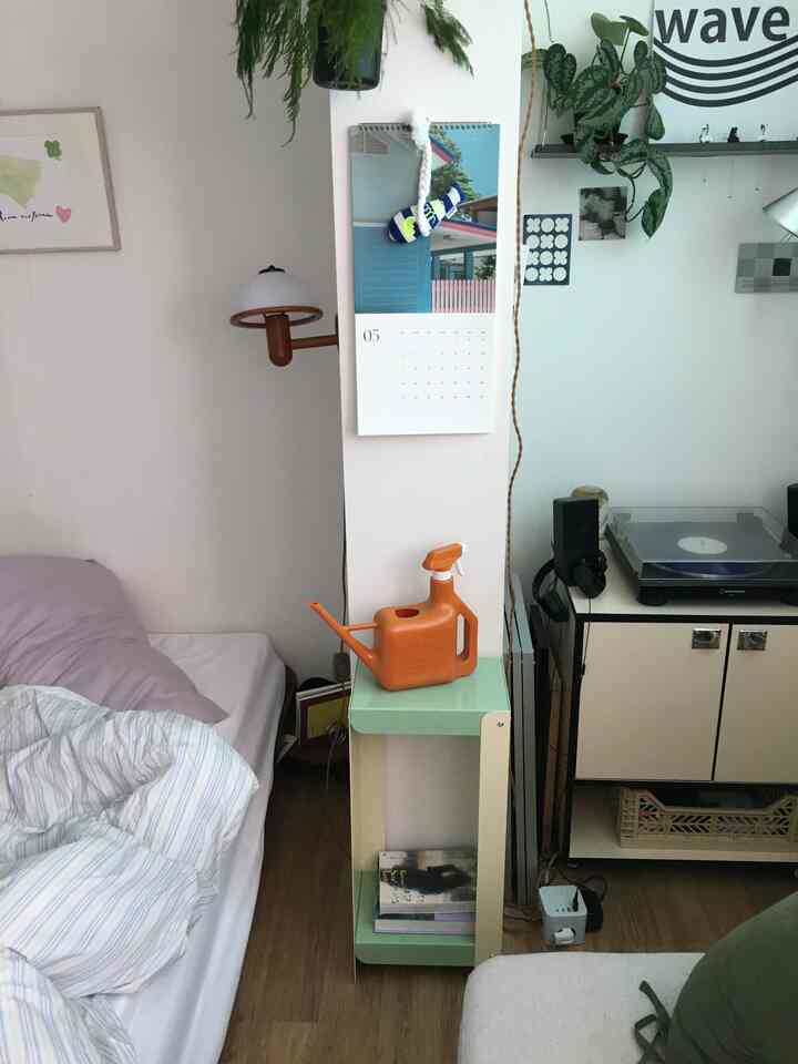 ナチュラルな色調の狭い寝室、ベッドと鉄製の棚、ターンテーブルが配置された雰囲気のある空間