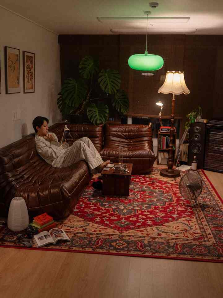 ブラウンとレッドのトーンのヴィンテージリビング、レザーソファとペルシャ絨毯、モンステラ植物、ヴィンテージ照明が配置された落ち着いた空間