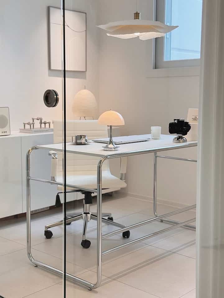 白とシルバーのトーンのホームオフィス、クロム脚のデスクとオフィスチェアが配置されたミッドセンチュリーモダンの雰囲気あるインテリア